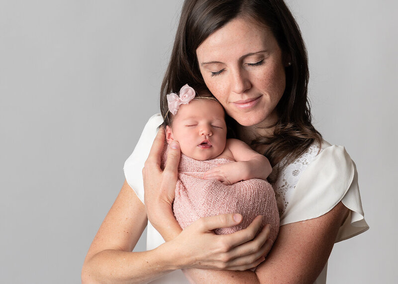 Mom holding newborn baby girl in pink wrap with eyes closed