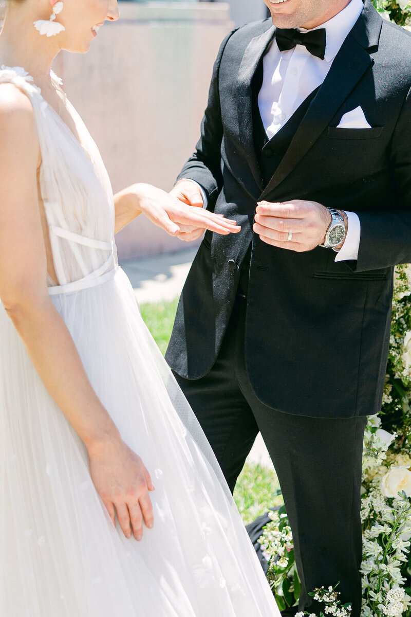 A groom in a classic black tuxedo places a ring on his bride’s finger during a Sarasota wedding, Amia Marcell Destination Wedding Photographer, Sarasota, Florida.
