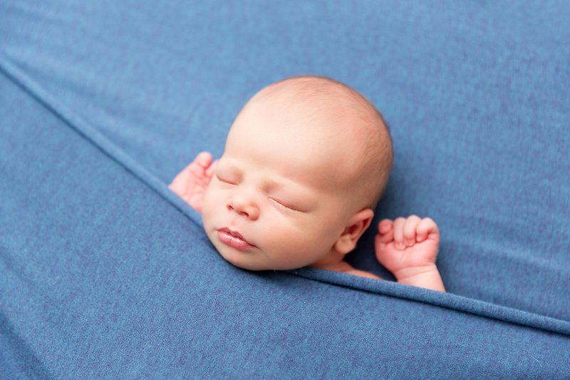 Newborn posed tucked in blue blanket