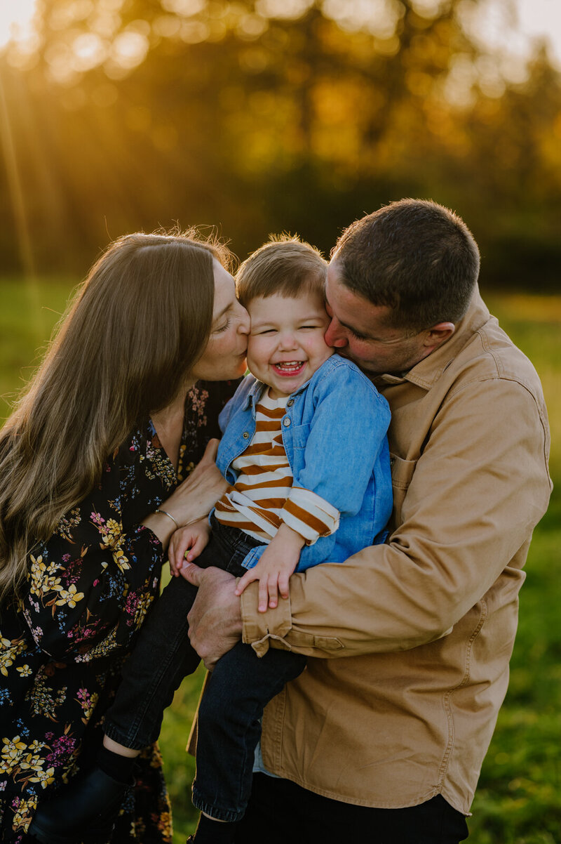 Portrait of a son being kissed on both cheeks by his parents and smiling.