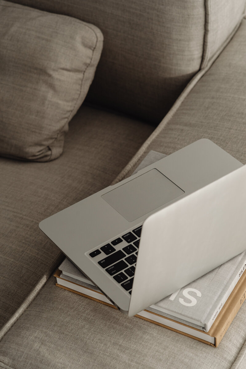 macbook laptop sitting on books on armrest of couch