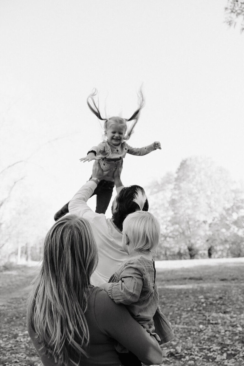Dad throws his daughter up in the air while mother and other daughter look on