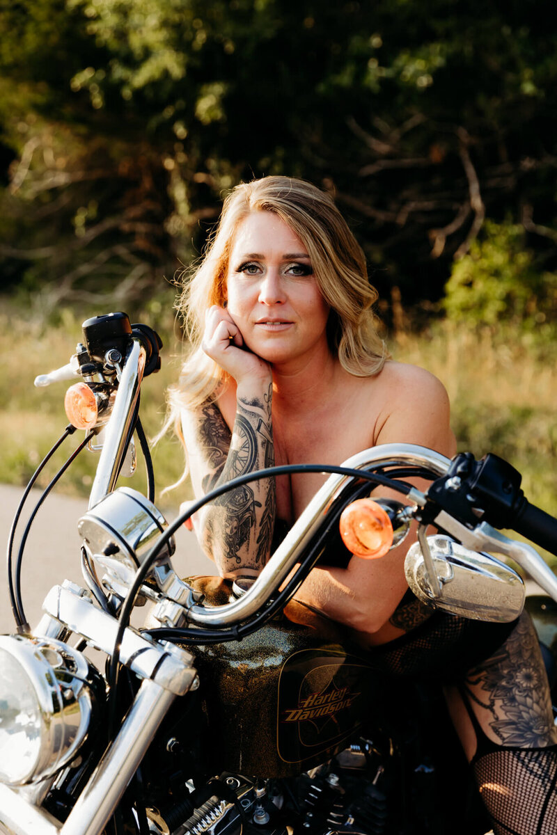 absolutely gorgeous woman with tattoos sitting on her motorcycle and looking over her handlebars during her boudoir photography session