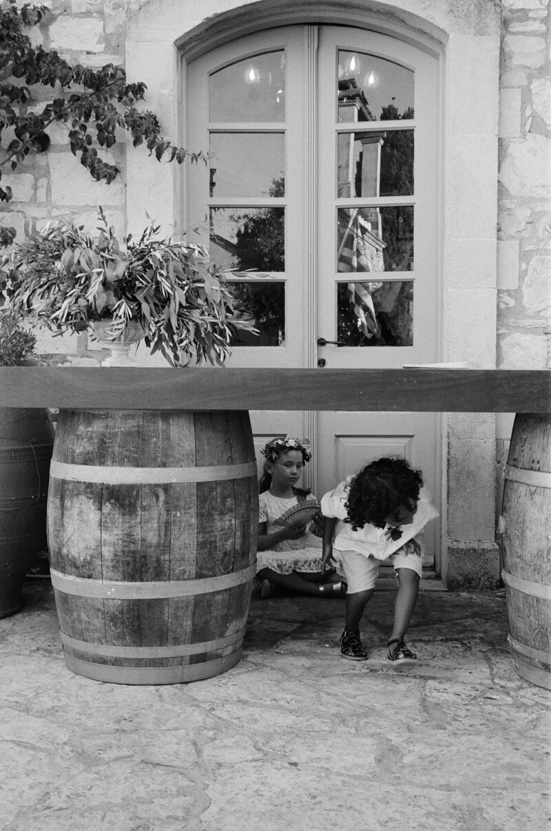Candid moment of children playing under a table during a joyful wedding celebration in Greece, capturing authentic family fun.