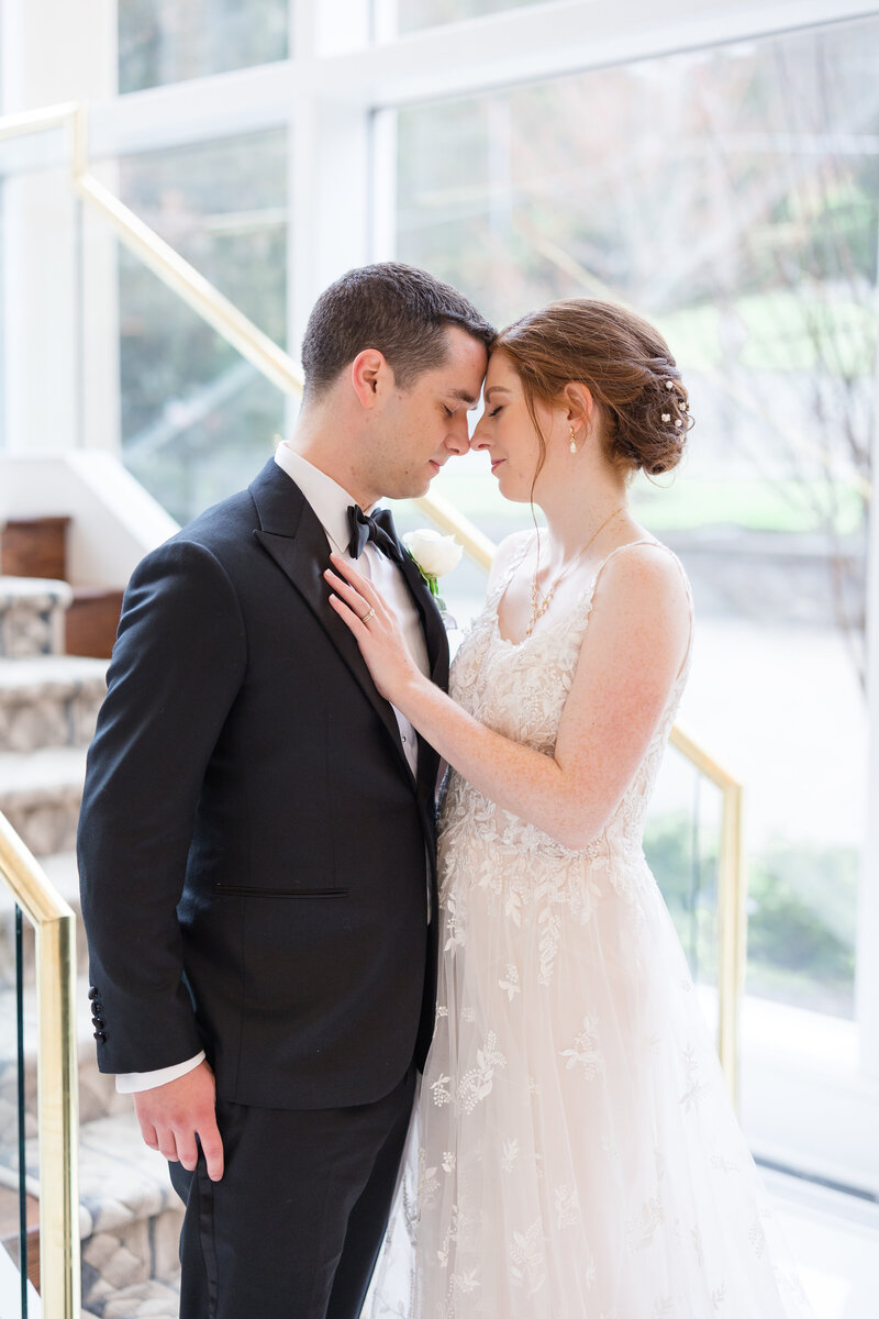 Newlyweds laugh and walk arm in arm under a bridge holding a white bouquet
