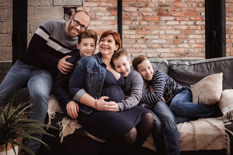 famille nombreuse souriante réunie sur un divan et entourant la maman enceinte 