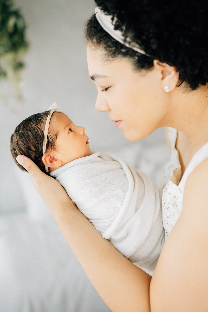 side profile of mother holding her swaddled newborn baby looking at each other