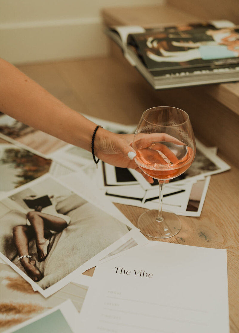 A wooden floor covered in editorial photos and a woman's hand holding a rose wine glass