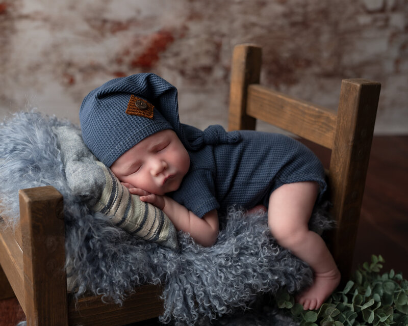 Baby boy in navy blue outfit posed on rustic newborn bed with soft blue textures in Paris, Ontario.