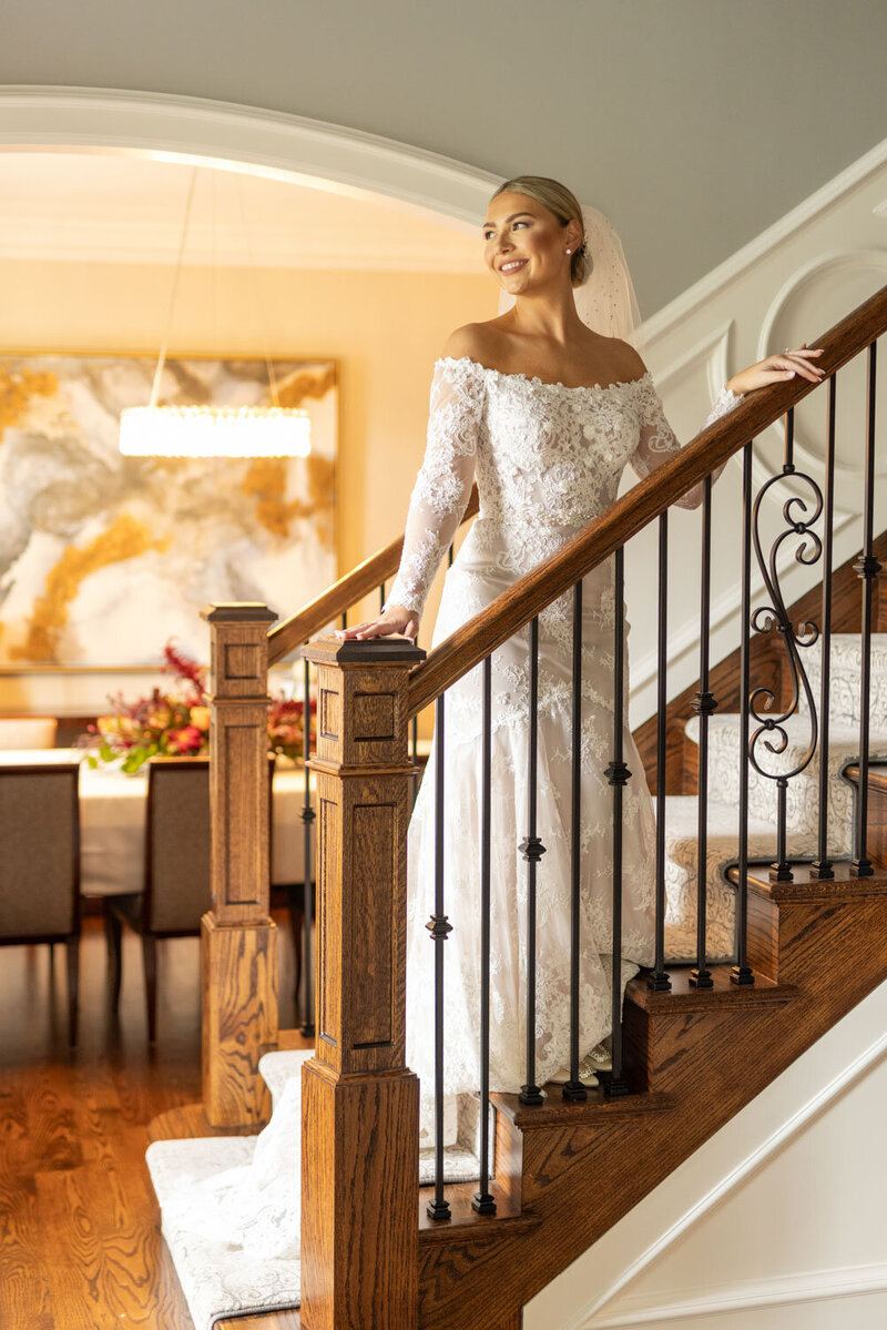 Bride in a lace off-shoulder gown standing on a wooden staircase