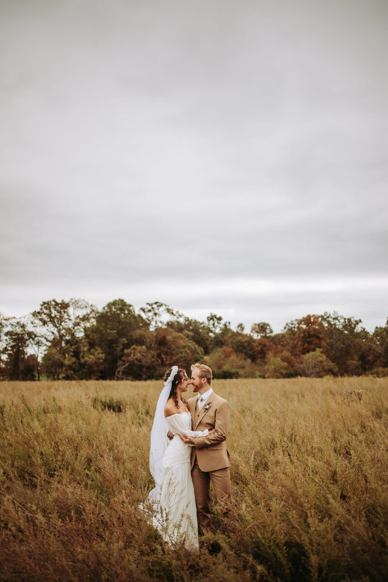 bride and groom touching noses in field