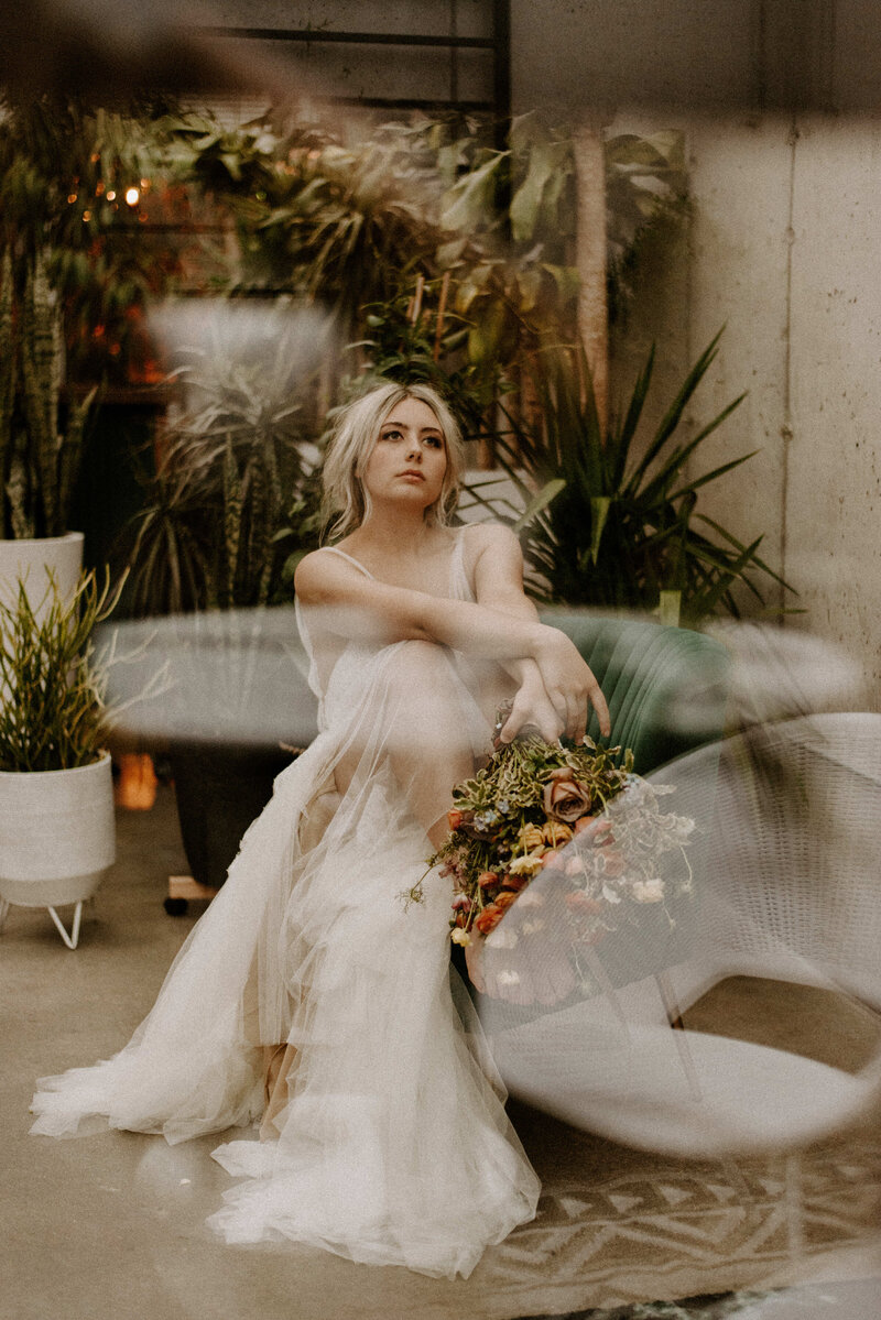 Indie bride sitting down surrounded by florals and plants