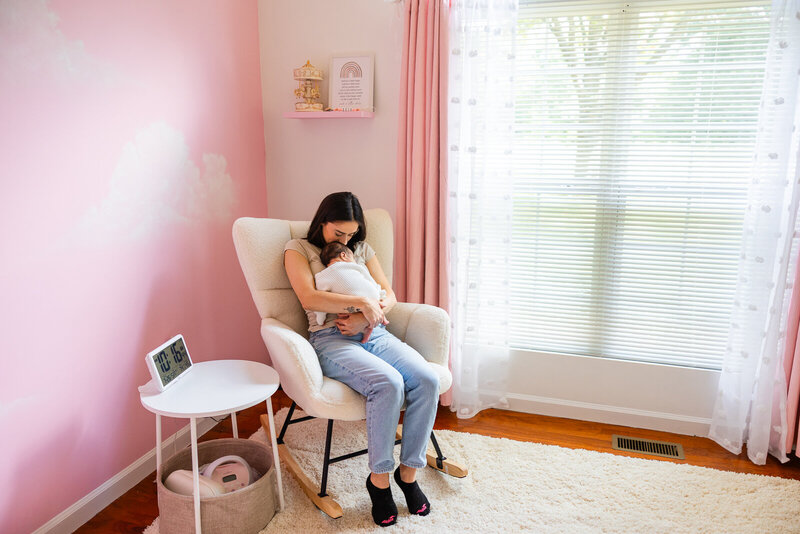 A mother rocking her infant in the nursery decorated with pink walls and hand painted clouds in DeSoto, Missouri. 