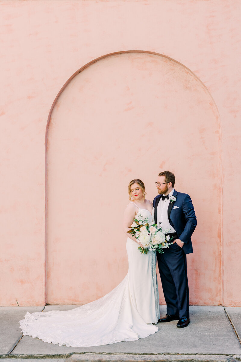 Bride and groom posting in front of a pink wall