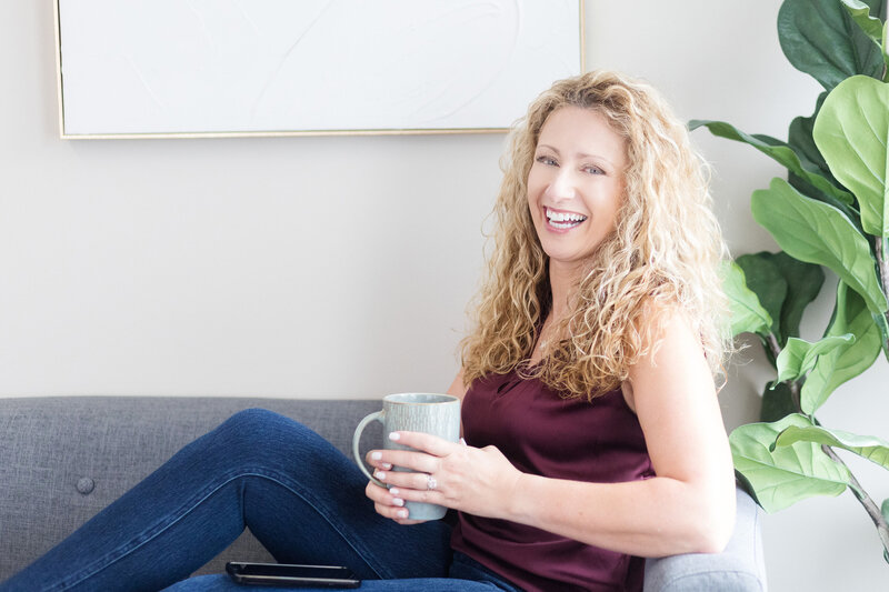 Kathleen sitting on a couch, holding a cup of coffee, smiling