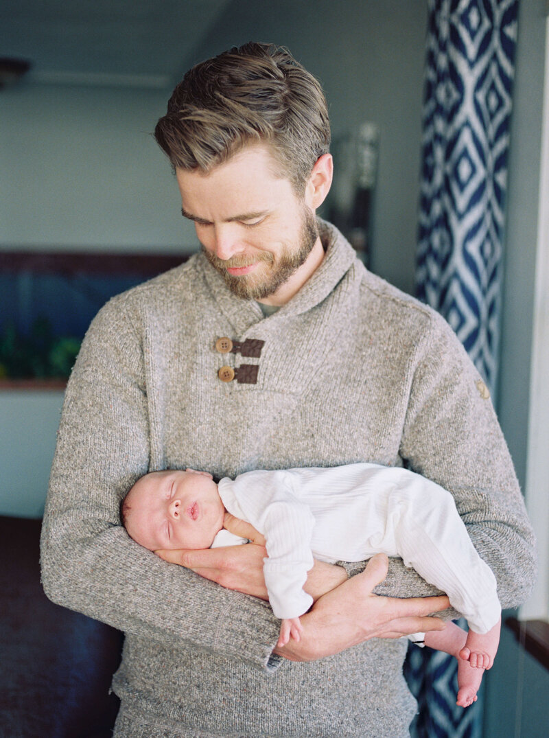 A new father holds his newborn baby and smiles at him during a family photographer session in the DMV