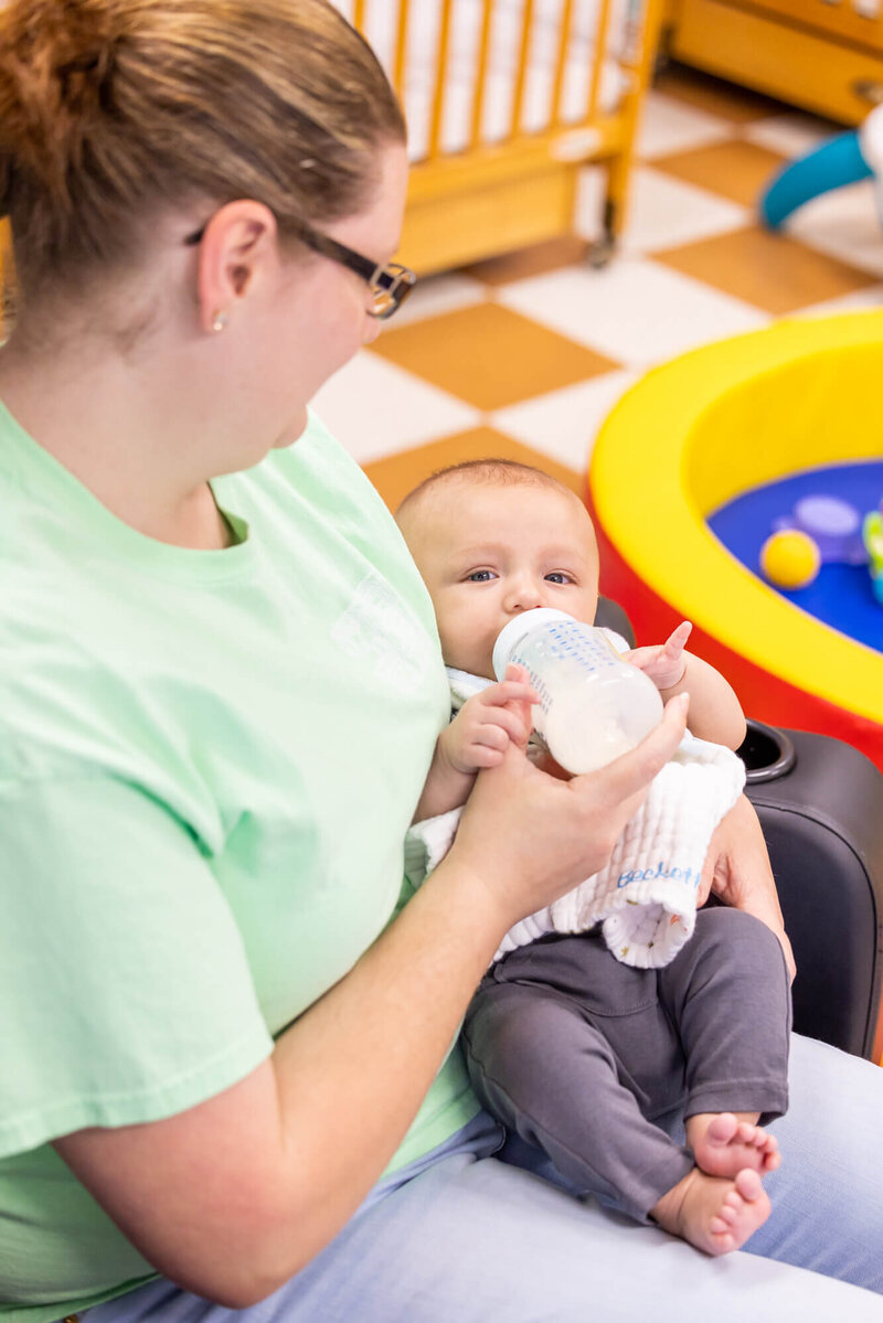 infant being held and fed with a bottle by a daycare worker