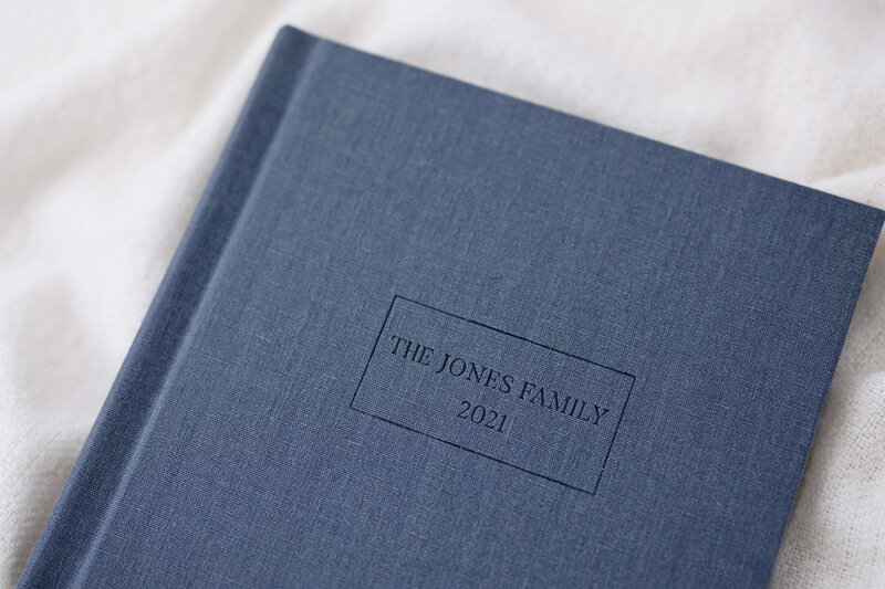 A navy blue engraved photo album that says "The Jones Family 2021" on it, against a white cloth background.