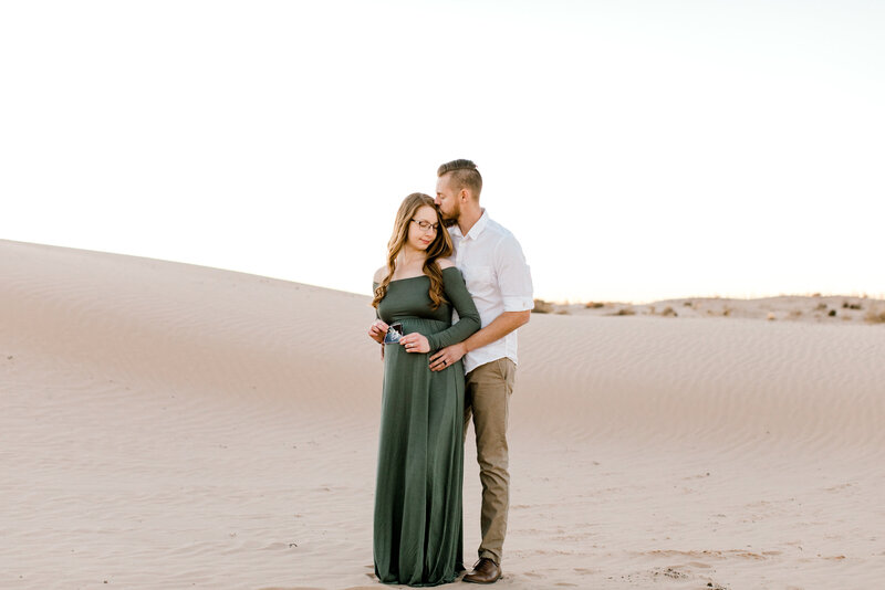 Maternity photo session on the sand hills near Lubbock Texas. Pregnant momma is wearing a green long sleeved dress pulled off the shoulders.