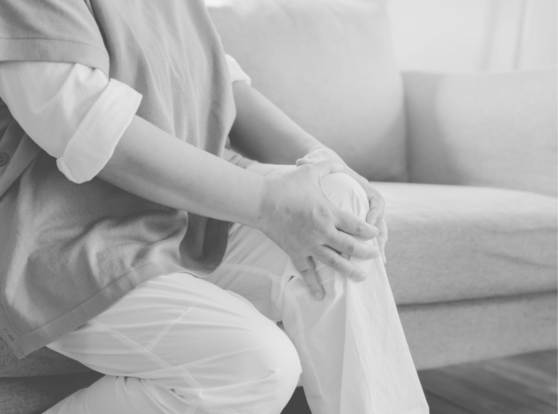 A person sits on the floor, holding their knee in discomfort, suggesting joint pain or injury.
