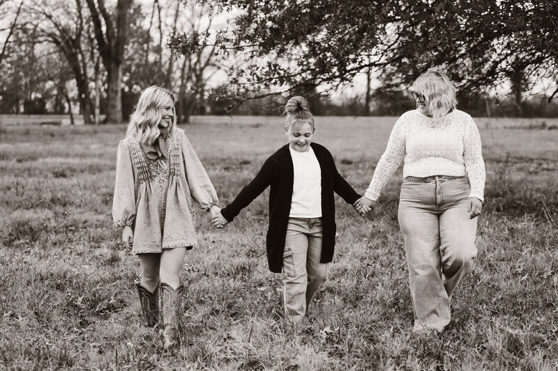 Black and white photo of three females walking hand-in-hand through a field