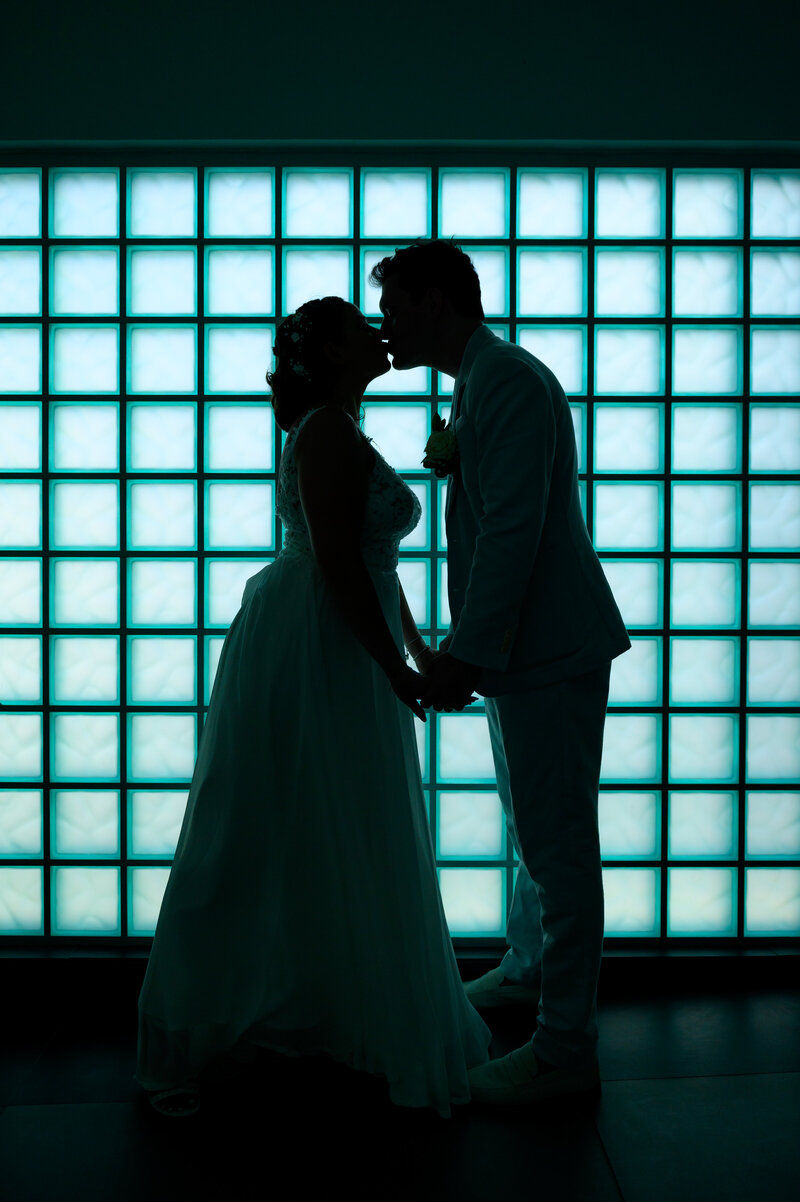 A bride and groom kissing in front of a glass wall at a resort in Aruba during a destination wedding.