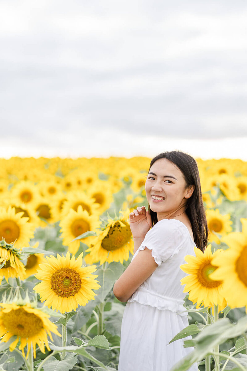 engaged girl in romantic white dress standing in sunflower field