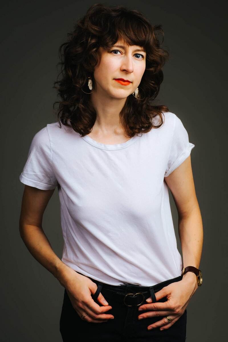 Studio self portrait of photographer Adrianne Mathiowetz, in a white t-shirt, black jeans and red lipstick.