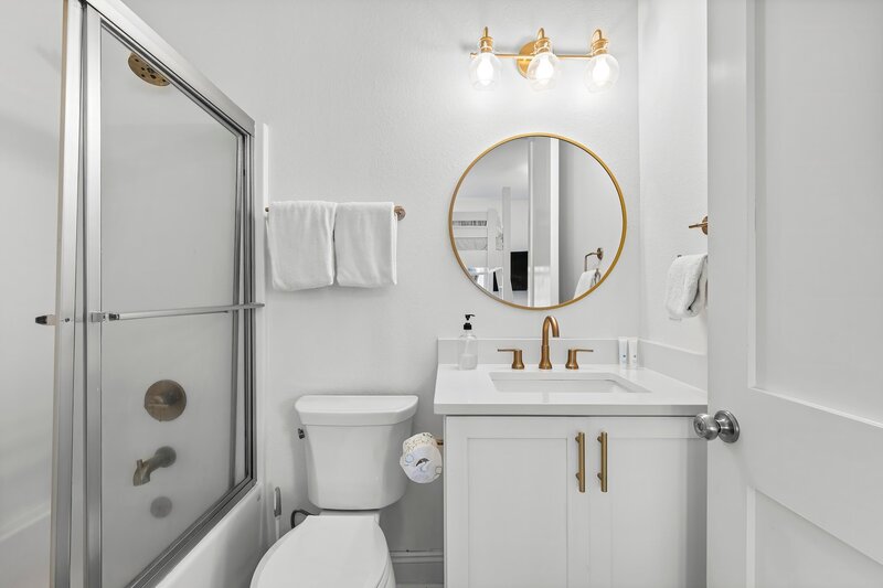Stylish full bathroom with round mirror, white vanity, and gold hardware—just off the upstairs bunk room in this colorful Panama City Beach retreat.