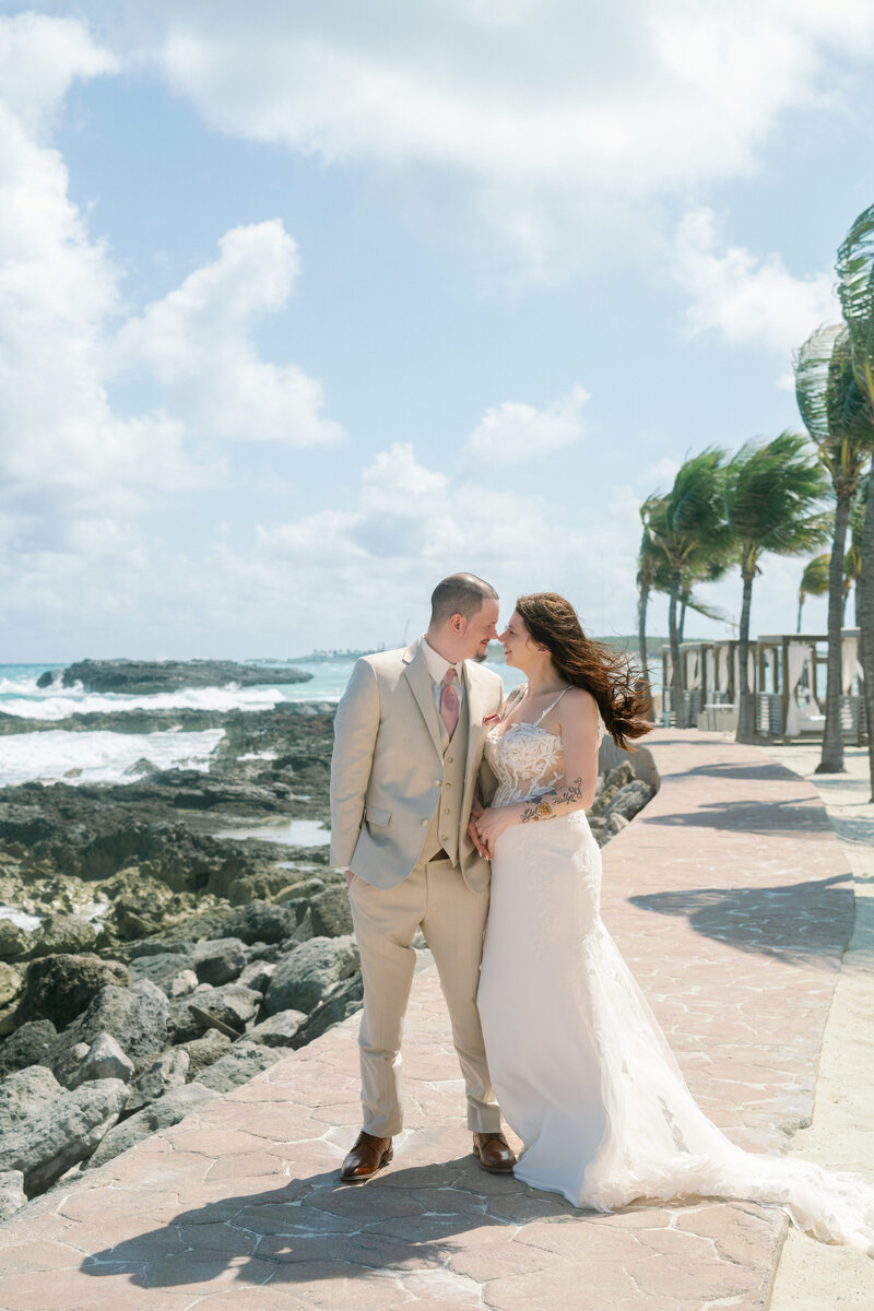 A bride and groom walk on a path by the ocean at their Royal Caribbean Cruise wedding