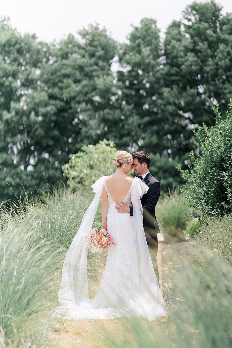 bridal photography with groom holding his bride around the waist and resting his forehead on her face while they are on a path surrounded by tall grass captured by Columbus wedding photographer
