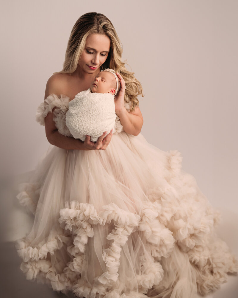 New Haven  newborn photographer captures a new mom wearing a gorgeous beige gown and holding her newborn baby girl in our Ct newborn studio.