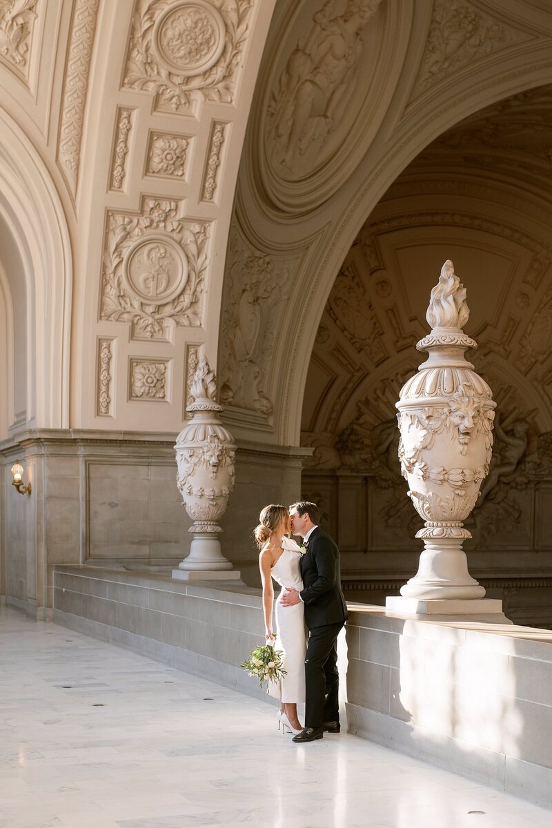 Bride and groom embrace and smile at each other in front of stone wall
