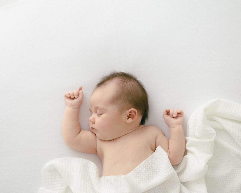baby with bow on her head smiling at camera in-home newborn photography session captured by Tampa lifestlyle photographer.