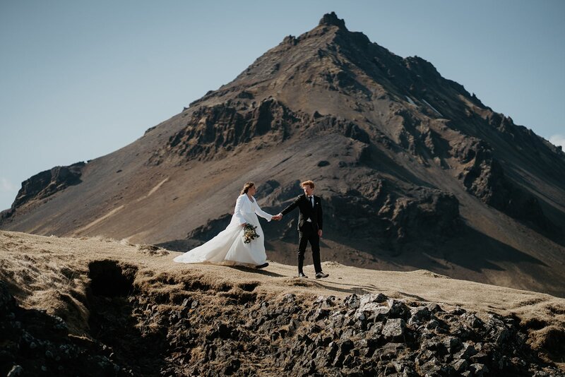Bride and groom hold hands while walking around a mountain trail during their Iceland elopement. 