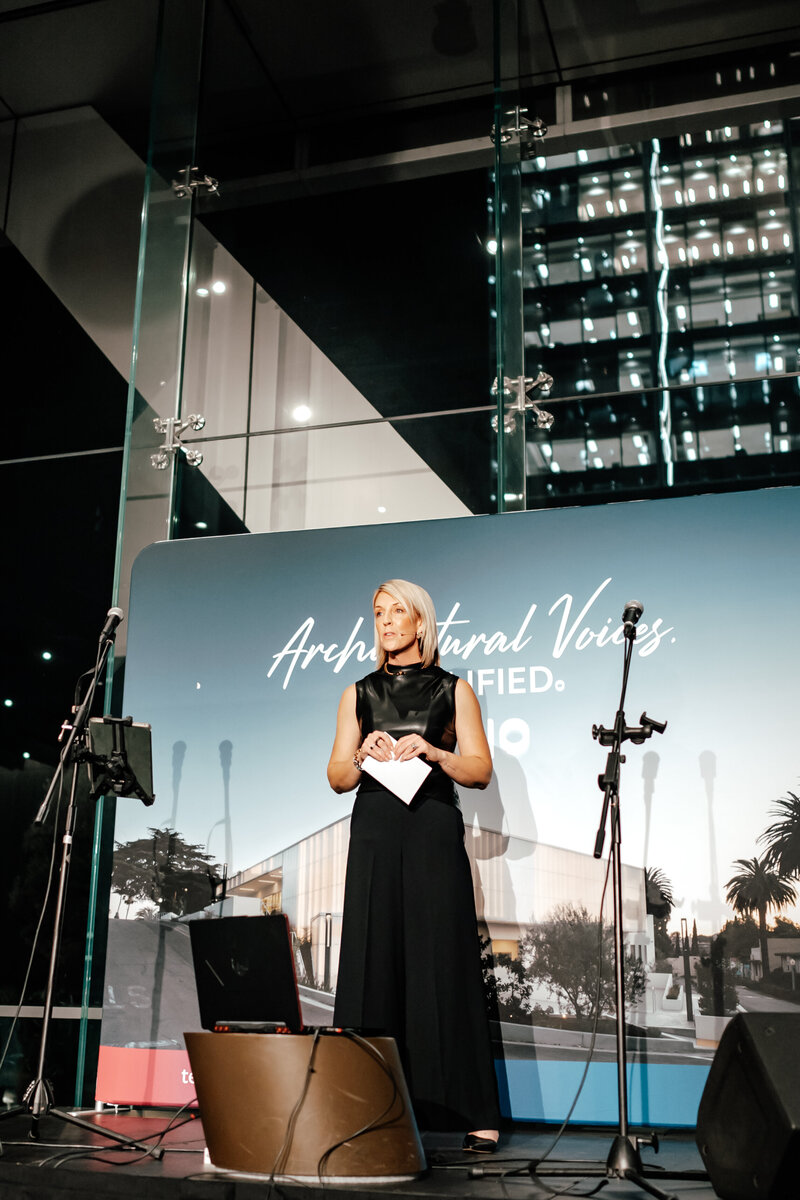 Woman standing on a stage at an architectural event in Auckland city talking to all the guests captured by Zanthe Vorsatz Photography 