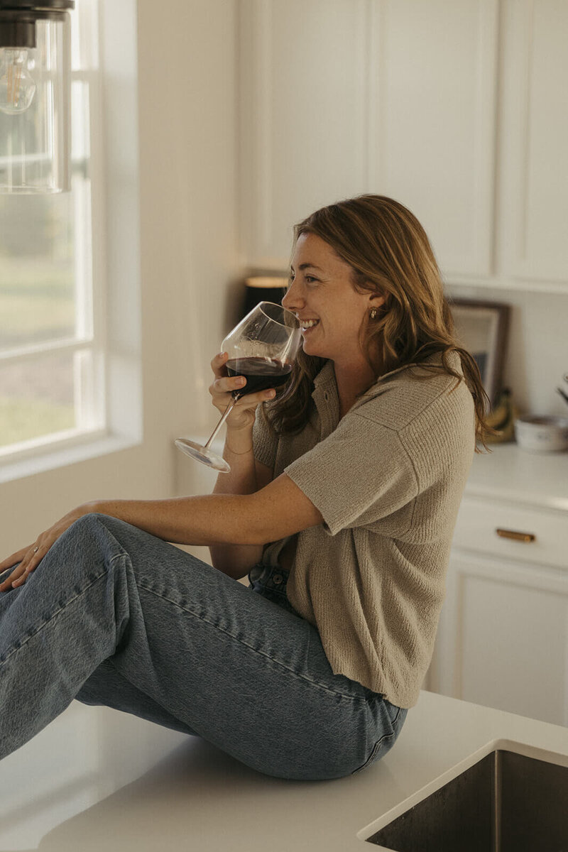 Wedding photographer sips her red wine while sitting on her kitchen counter