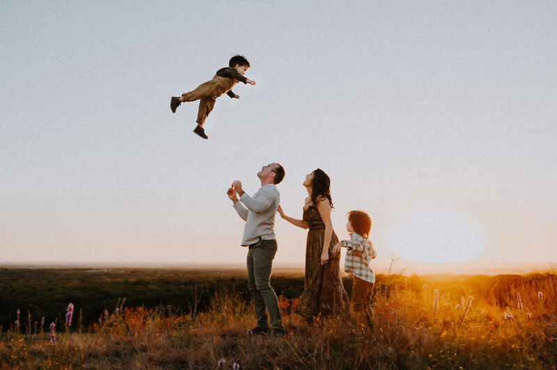 A father tossing his toddler in the air to catch him while the mother looks on with a smile in Decatur, tx
