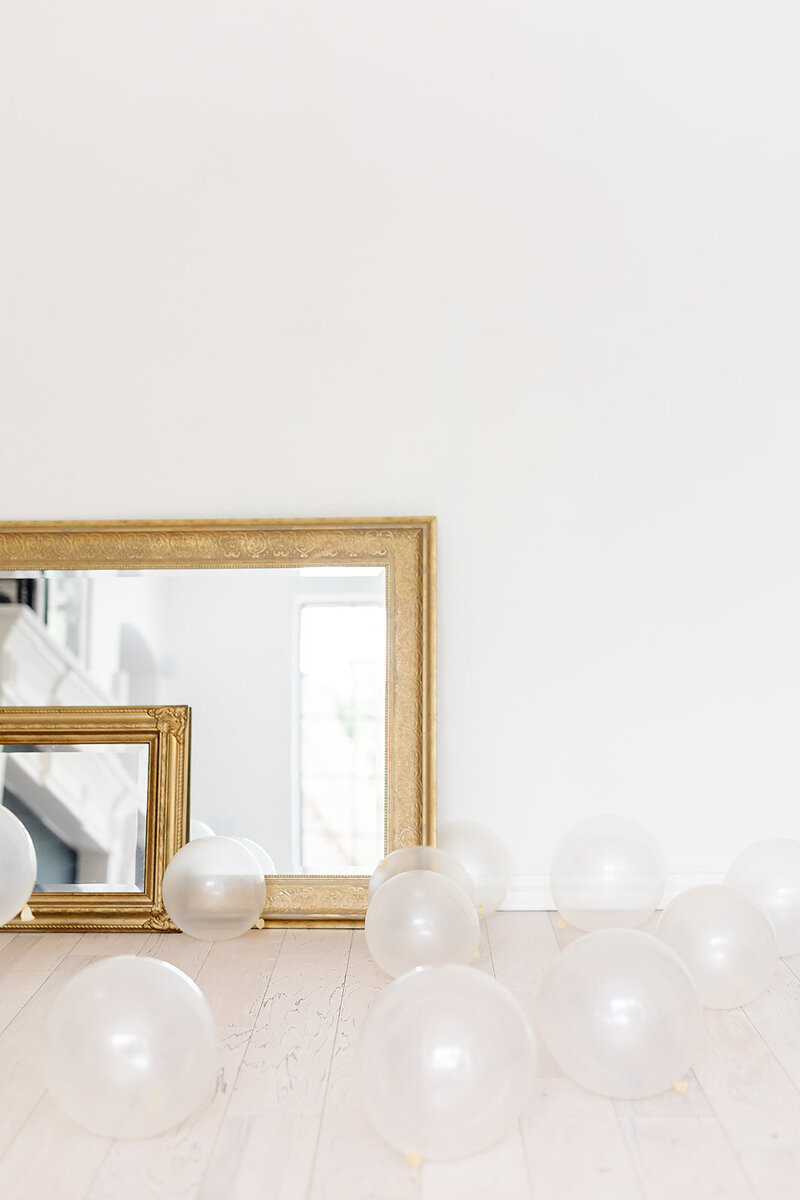 Gold mirror and clear balloons sitting on the floor in front of a white wall