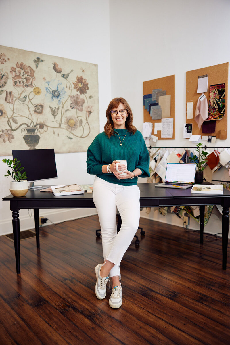 Jackie Barnes, interior designer standing in front of her desk with a cup of coffee.