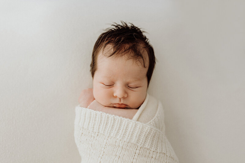 A newborn baby with dark brown hair sleeping while posed for newborn portraits with Christchurch photographer Lucy Jane Photography