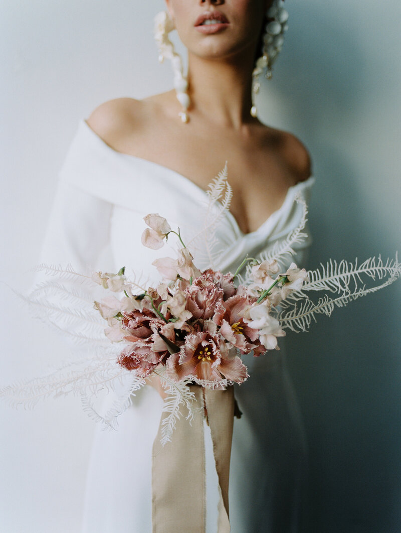 Young bride wearing off sleeve white wedding gown holding pink bouquet