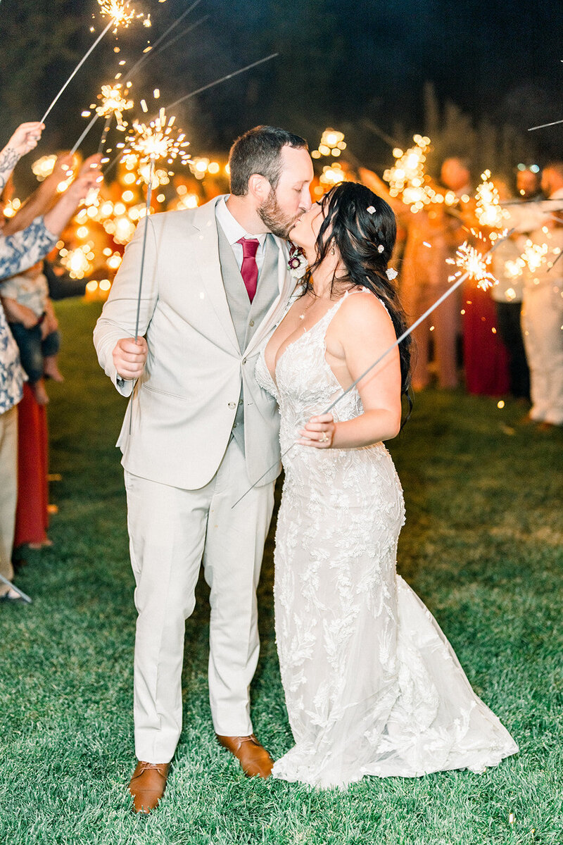 Tiffany Longeway Photography captures the magic of a romantic sparkler exit at Viansa Sonoma Winery. The bride and groom share a kiss surrounded by friends and family, illuminated by the glow of sparklers, creating an unforgettable moment. Ideal for couples seeking a luxurious and festive wedding celebration in Sonoma’s picturesque wine country.