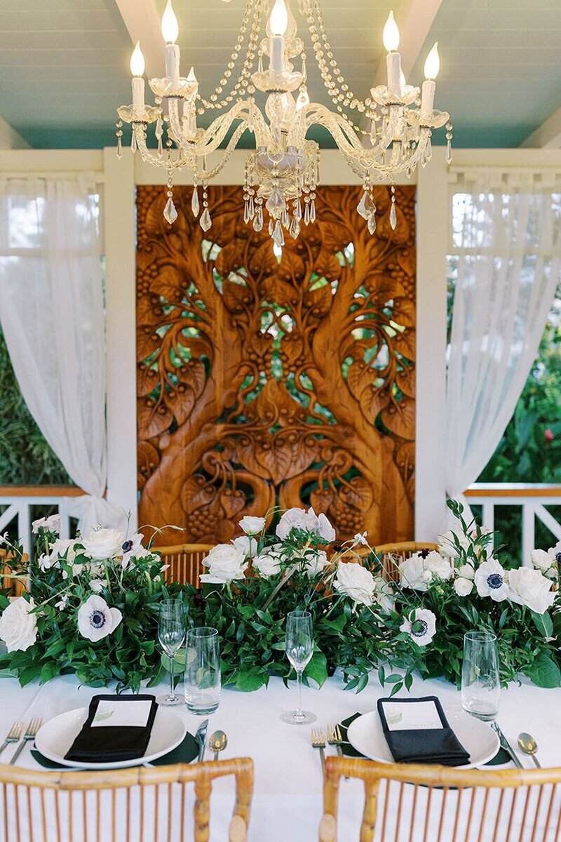 Wedding reception table featuring rich wood elements, complemented by lush green and white florals.