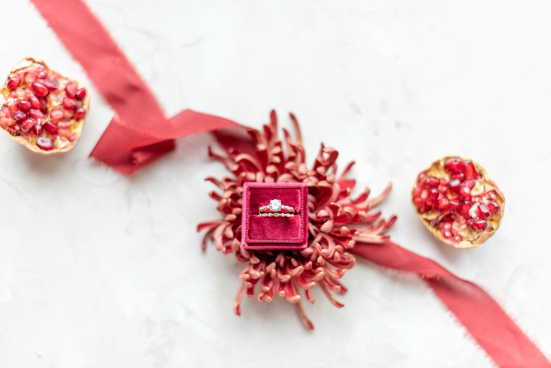 wedding ring in maroon ring box with pomegranates and red ribbon
