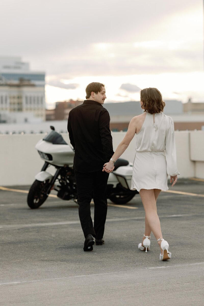 A couple walks away from the camera towards a motorcycle.