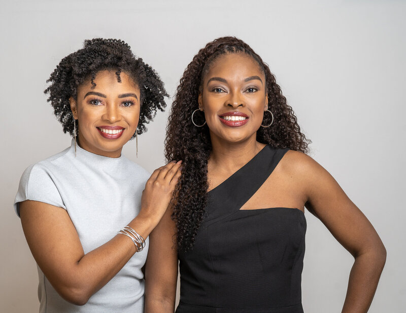 Two African American women smile into the camera while holding camera equipment