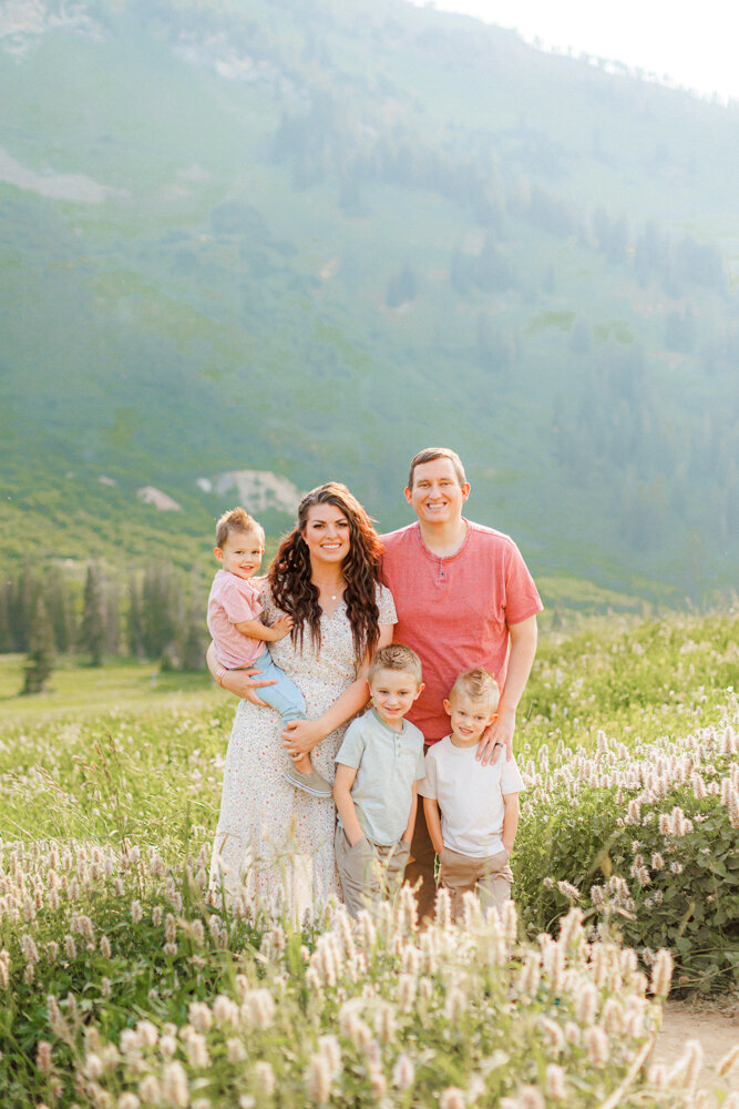 Cute family with three little boys stands and smiles for a portrait surrounded by gorgeous flowers and mountain backgrounds.