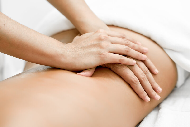 Massage therapist applying gentle pressure to a postpartum client’s lower back for recovery and relief.