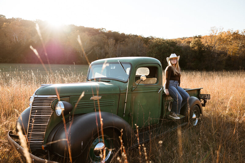 High school senior sitting on a green vintage truck in a field. 